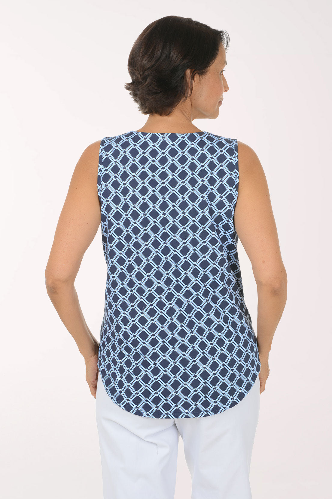 A woman modeling a sleeveless top with a navy blue and white geometric trellis pattern, featuring a split neckline and keyhole cutout, paired with white pants against a plain white studio background.