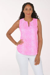 A woman modeling a sleeveless pink top with a white abstract pattern and a split neckline, paired with white pants, against a plain white background.