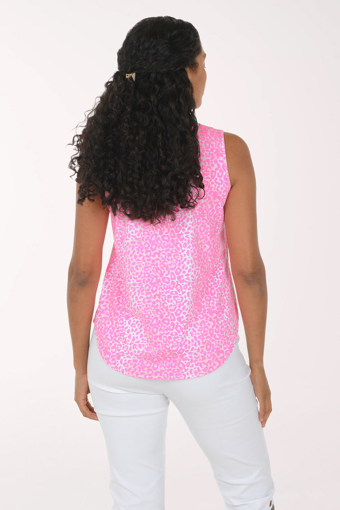 A woman modeling a sleeveless pink top with a white abstract pattern and a split neckline, paired with white pants, against a plain white background.
