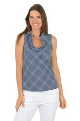Woman wearing a blue patterned sleeveless top and white pants on a white background.