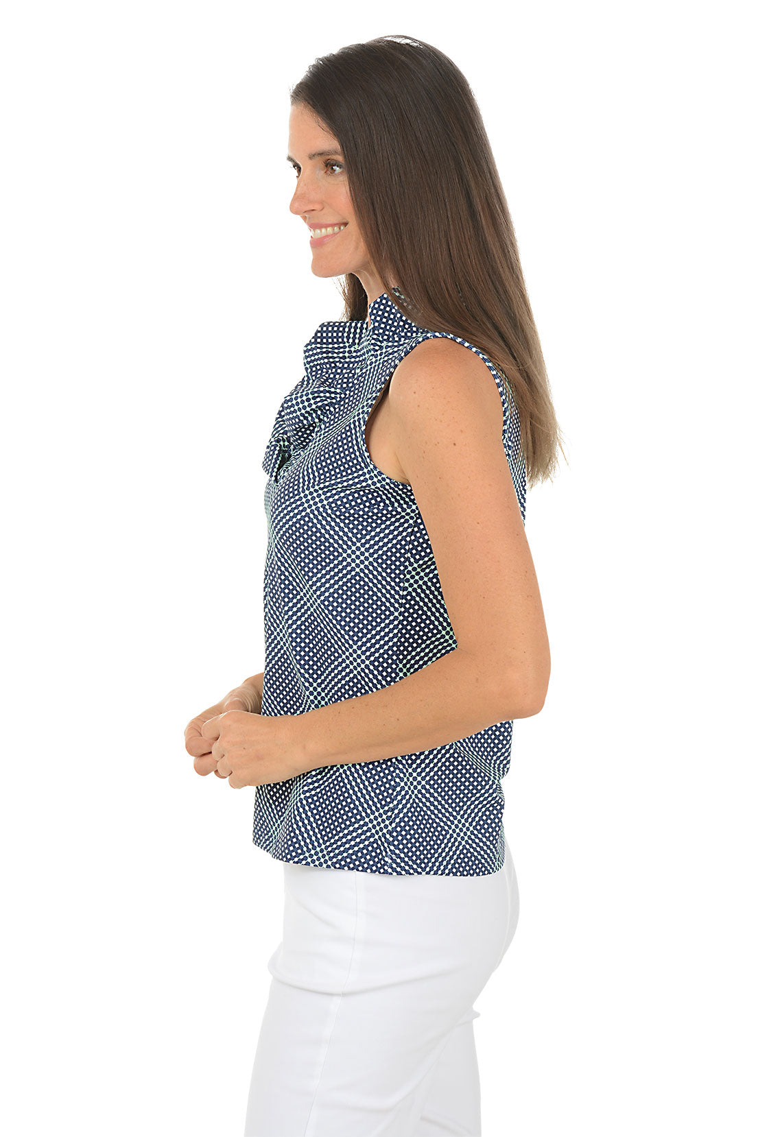 Woman wearing a blue patterned sleeveless top and white pants on a white background. Side shot.