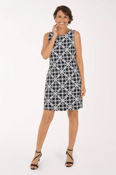 A woman modeling a sleeveless knee-length shift dress with a black and white geometric interlocking circle pattern, paired with black strappy high-heeled sandals against a plain white studio background.
