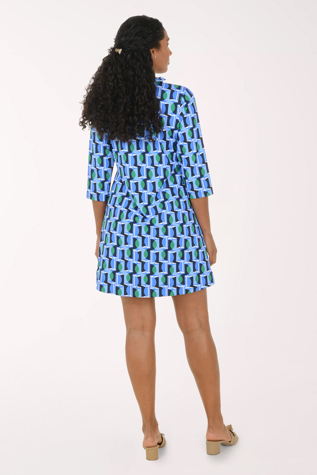 A woman modeling a short-sleeve button-up shirt dress with a blue, green, and white geometric pattern, standing against a plain white studio background.