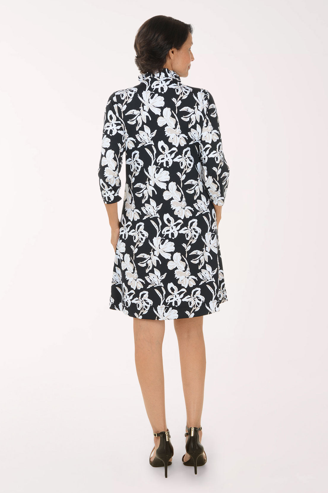 A woman modeling a black and white floral print shirt dress with three-quarter sleeves and a collared neckline, paired with black strappy high-heeled sandals against a plain white studio background.