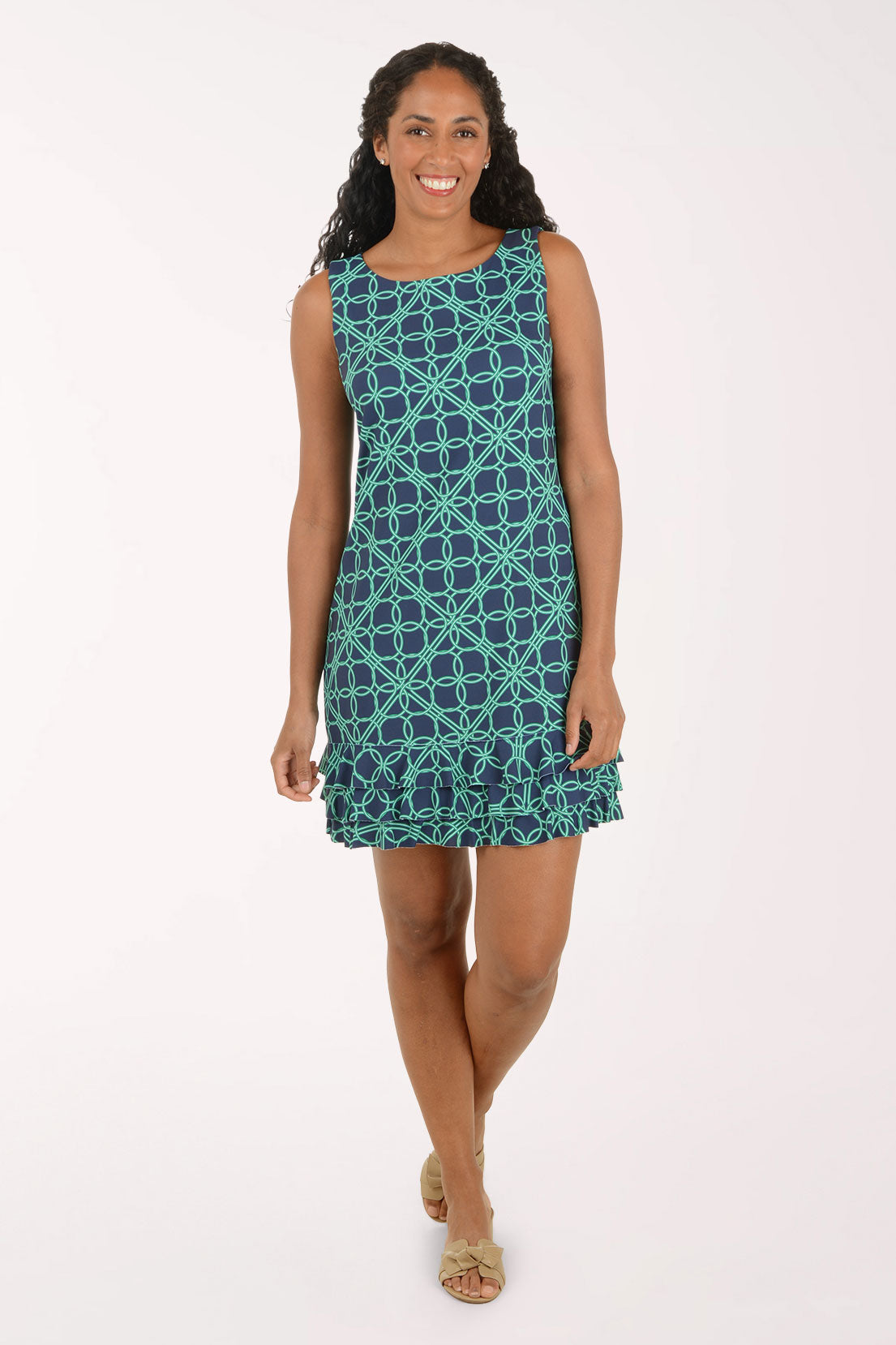 A woman modeling a sleeveless shift dress with a teal and navy geometric pattern, standing against a plain white studio background.