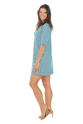 Woman wearing a blue patterned dress on a white background. Side shot.