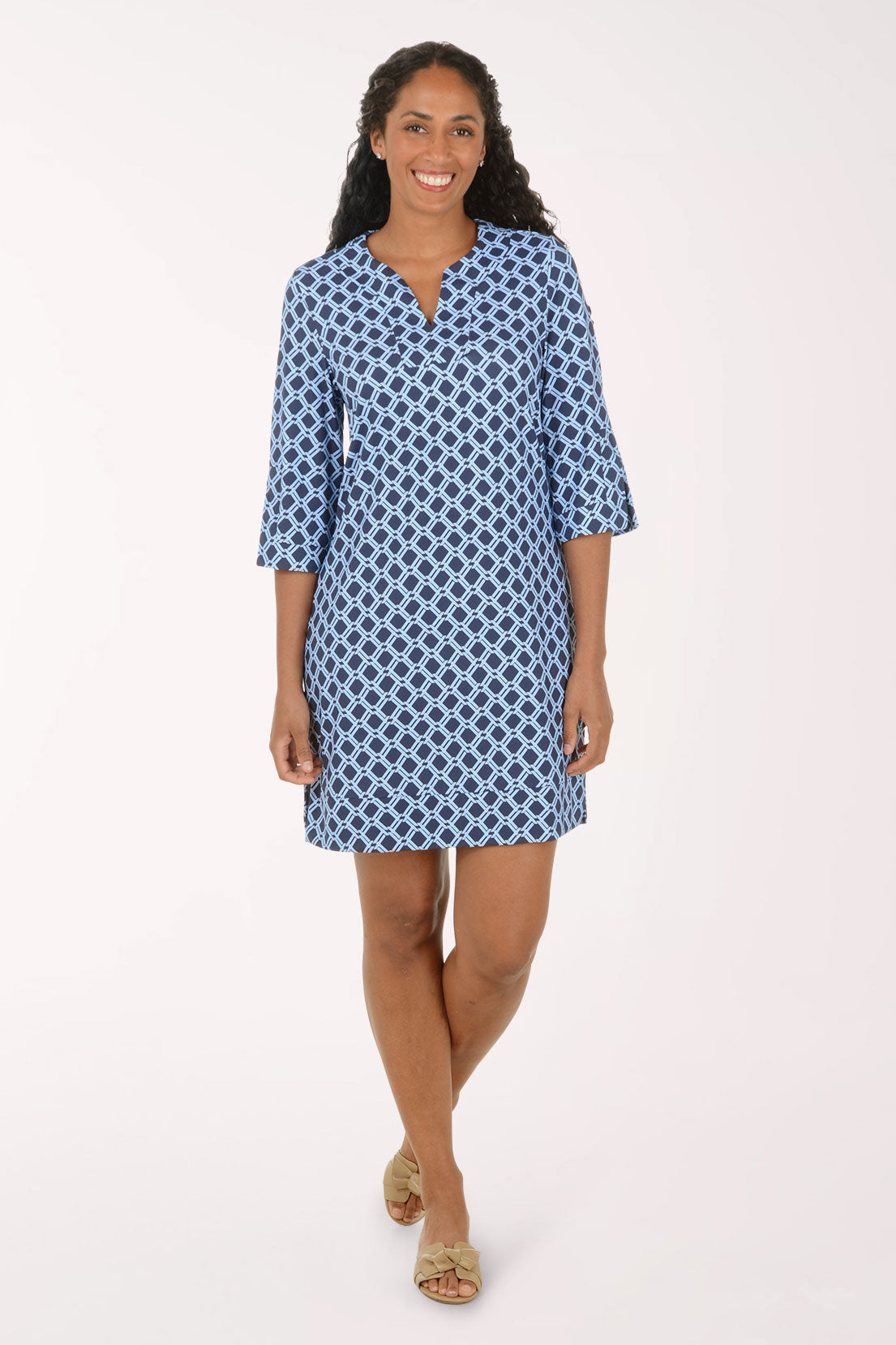 A woman modeling a short blue and white patterned tunic dress with three-quarter sleeves and a split neckline, standing against a plain light background.