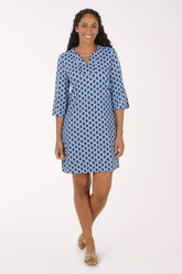 A woman modeling a short blue and white patterned tunic dress with three-quarter sleeves and a split neckline, standing against a plain light background.
