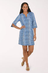 A woman modeling a short blue and white patterned dress with elbow-length sleeves and a split neckline, standing against a plain light background.