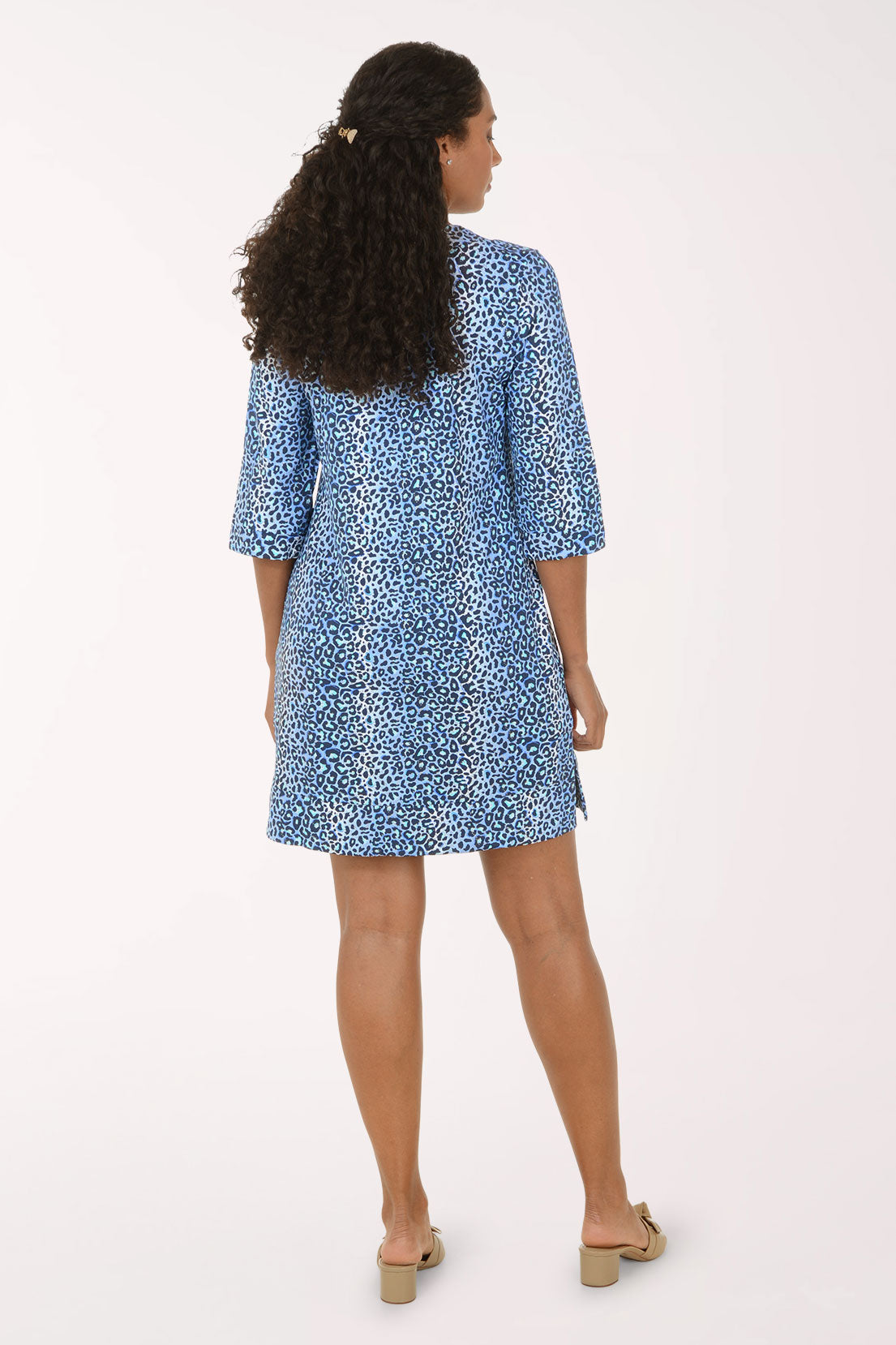 A woman modeling a short blue and white patterned dress with elbow-length sleeves and a split neckline, standing against a plain light background.