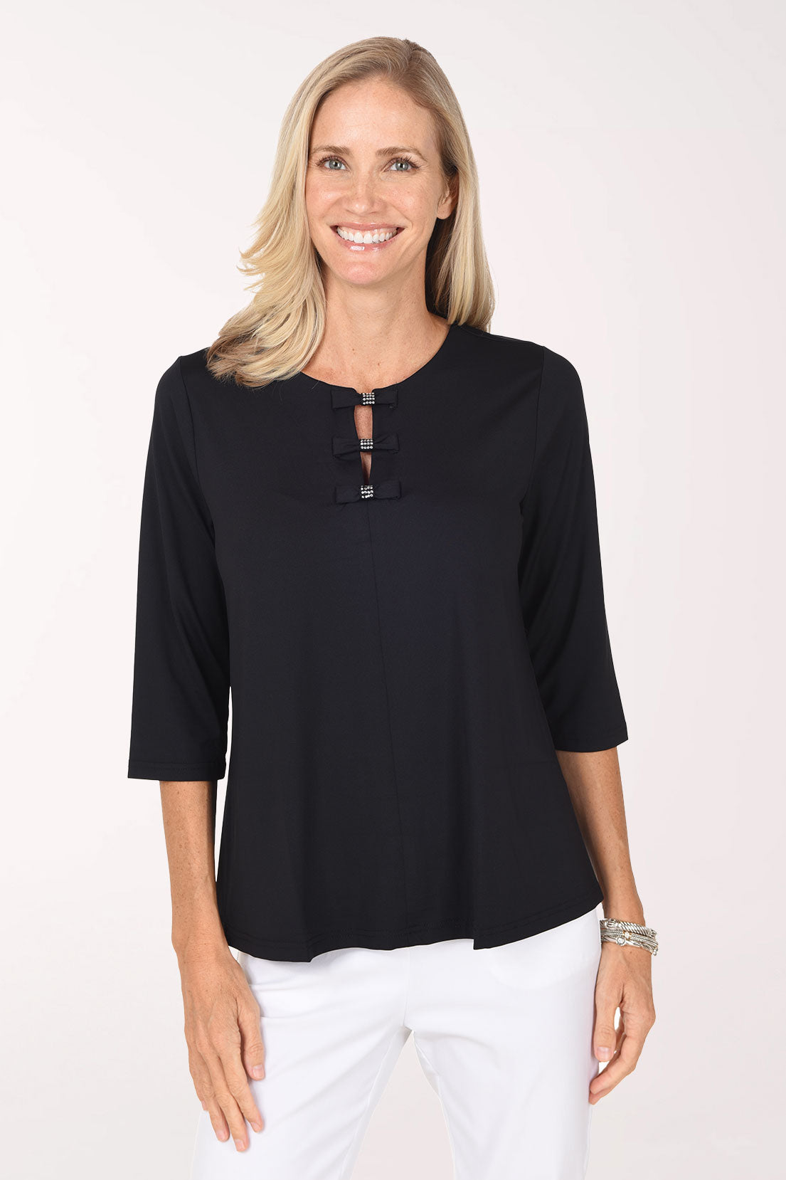 Front view of a model wearing the Anthony's Resort Wear Crystal Bow UPF50+ 3/4 Sleeve Top in black, with three small crystal-accented bows down the split neckline, worn with white pants.