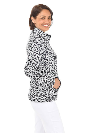 A woman wearing a black and white leopard-spotted zip front jacket and white pants in front of a white background. Side shot.