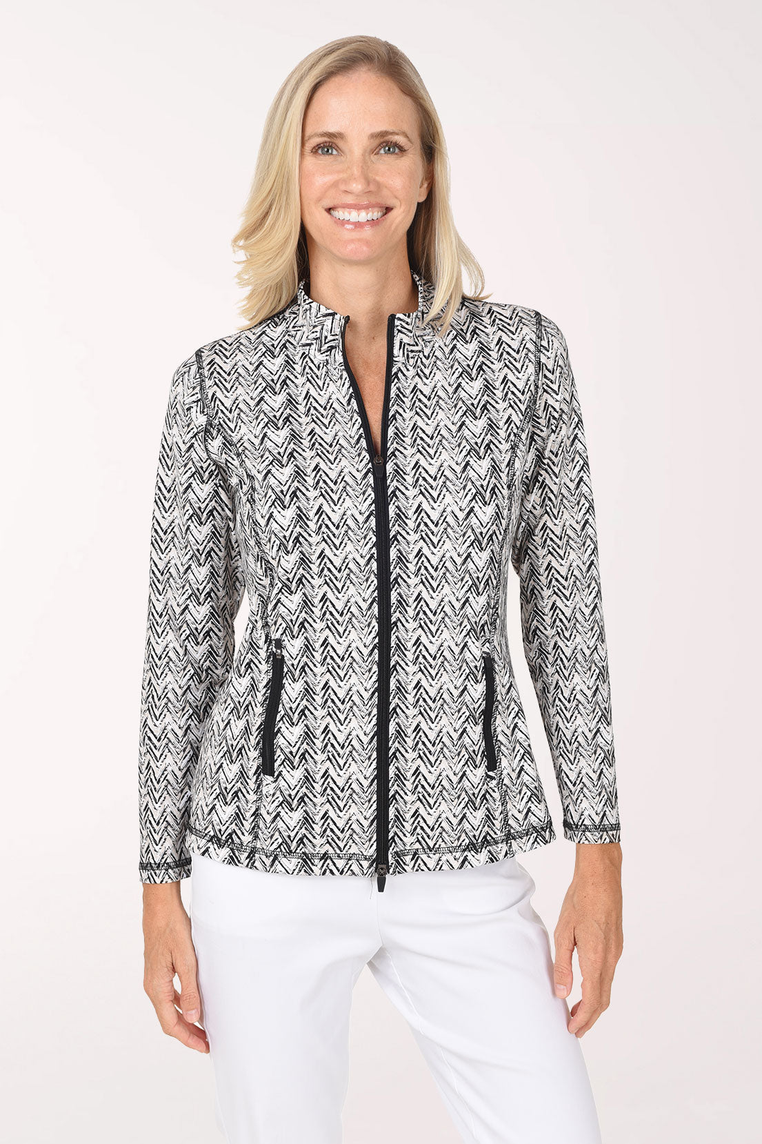 Front view of a model wearing the Anthony's Resort Wear Neutral Chevron UPF50+ Athletic Zip Jacket in a black and white brushstroke chevron print, with a black front zipper, black zip hip pockets and mock neck, worn with white pants.