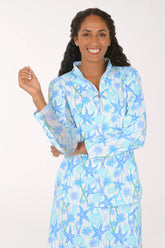 A smiling woman wearing a matching two-piece lounge set with a light blue and white starfish and palm tree print, featuring a long-sleeve quarter-zip top and a matching skirt.