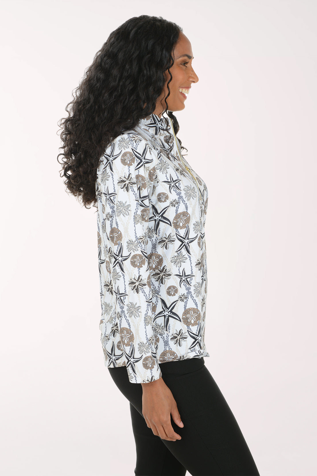 A woman shown in side profile wearing a white long-sleeve button-up shirt with a black and brown botanical and starfish pattern, paired with black pants, against a plain light background.