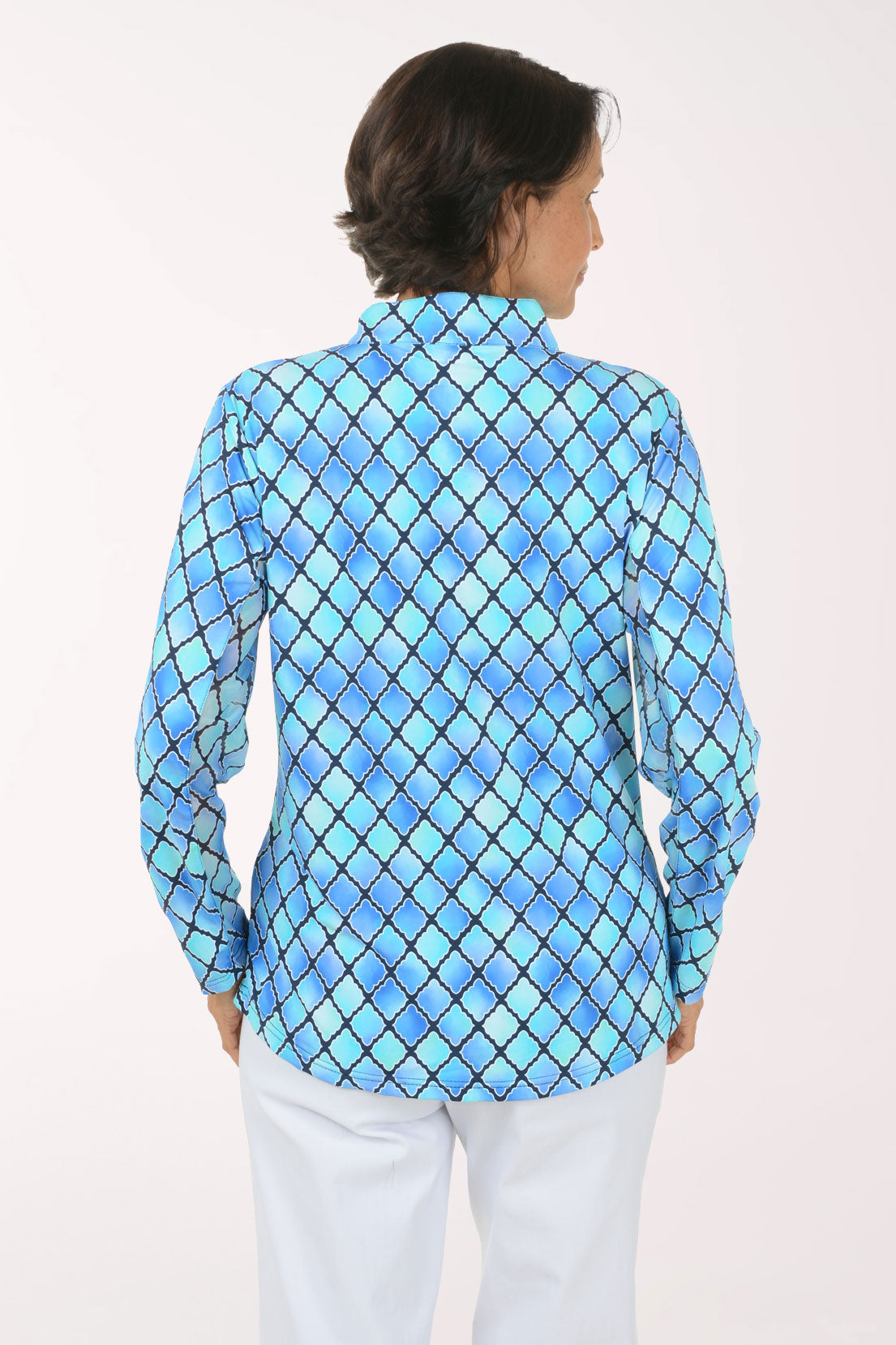 A woman modeling a blue and light blue diamond-patterned quarter-zip pullover top with white pants, set against a plain white studio background.
