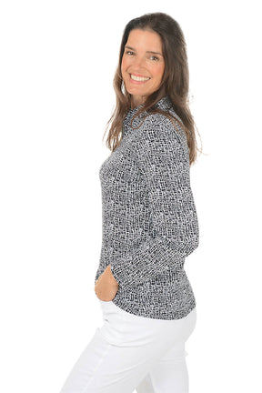 Woman wearing a black and white patterned blouse with white pants on a white background