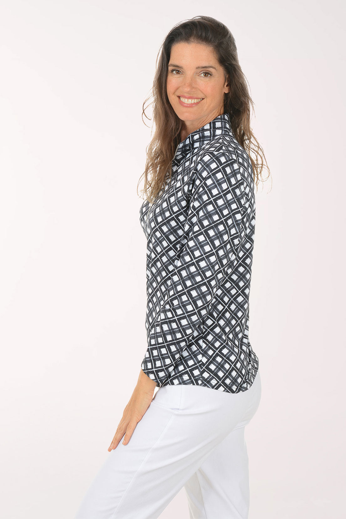 Woman wearing a patterned long-sleeve shirt and white pants on a light pink background