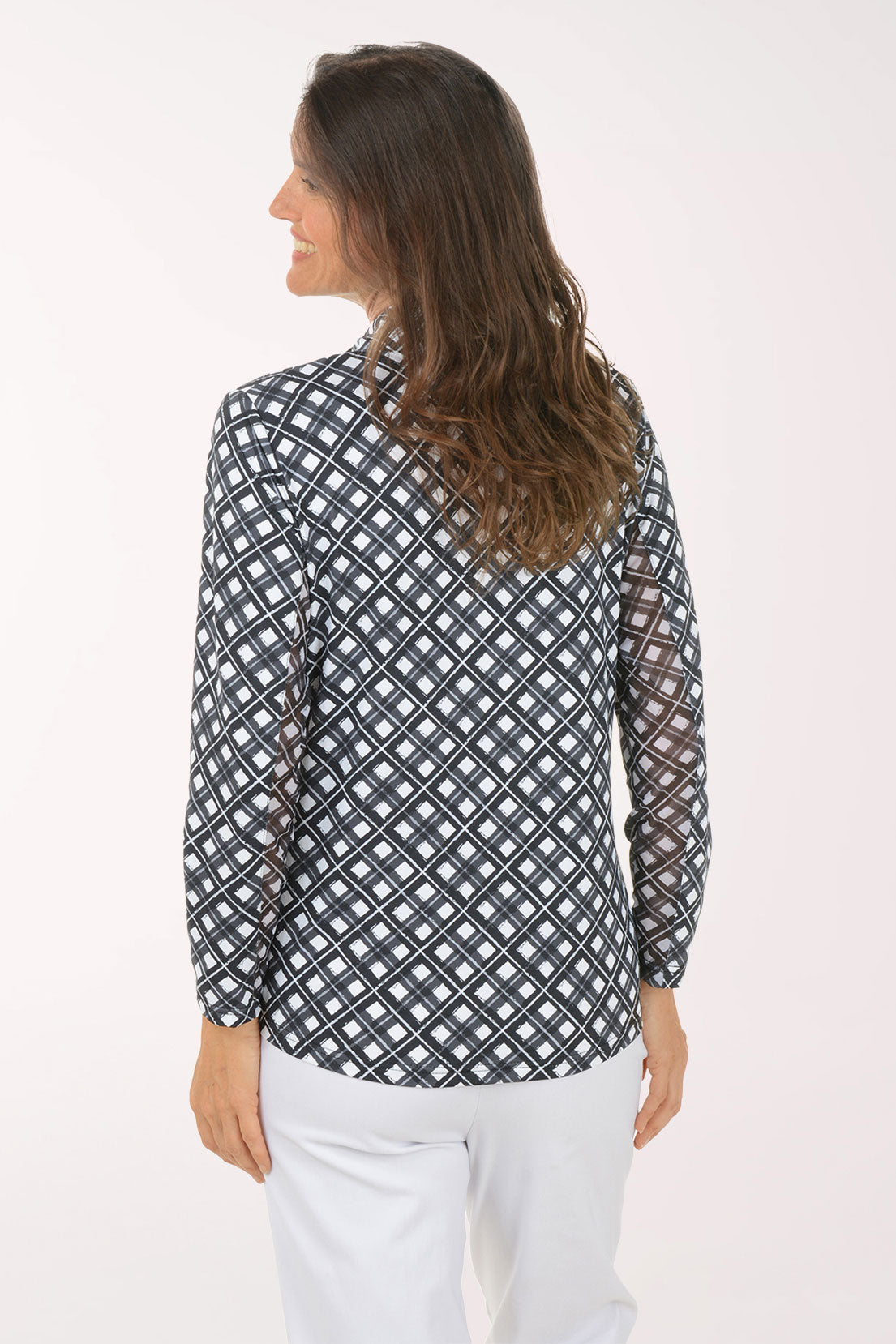 Woman wearing a patterned long-sleeve shirt and white pants on a light pink background