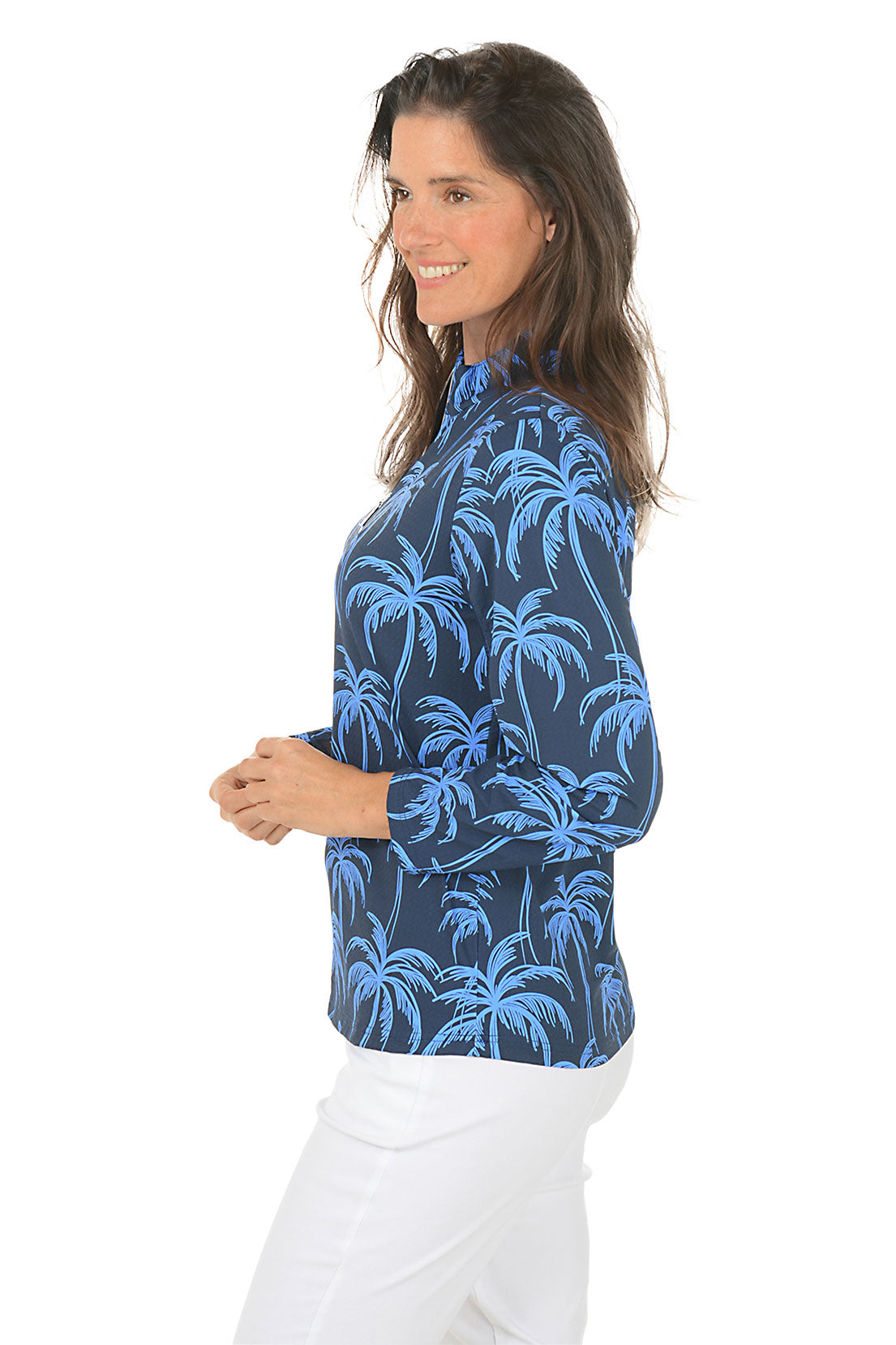 Woman wearing a blue palm tree patterned shirt on a white background. Side shot.