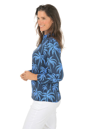 Woman wearing a blue palm tree patterned shirt on a white background. Side shot.