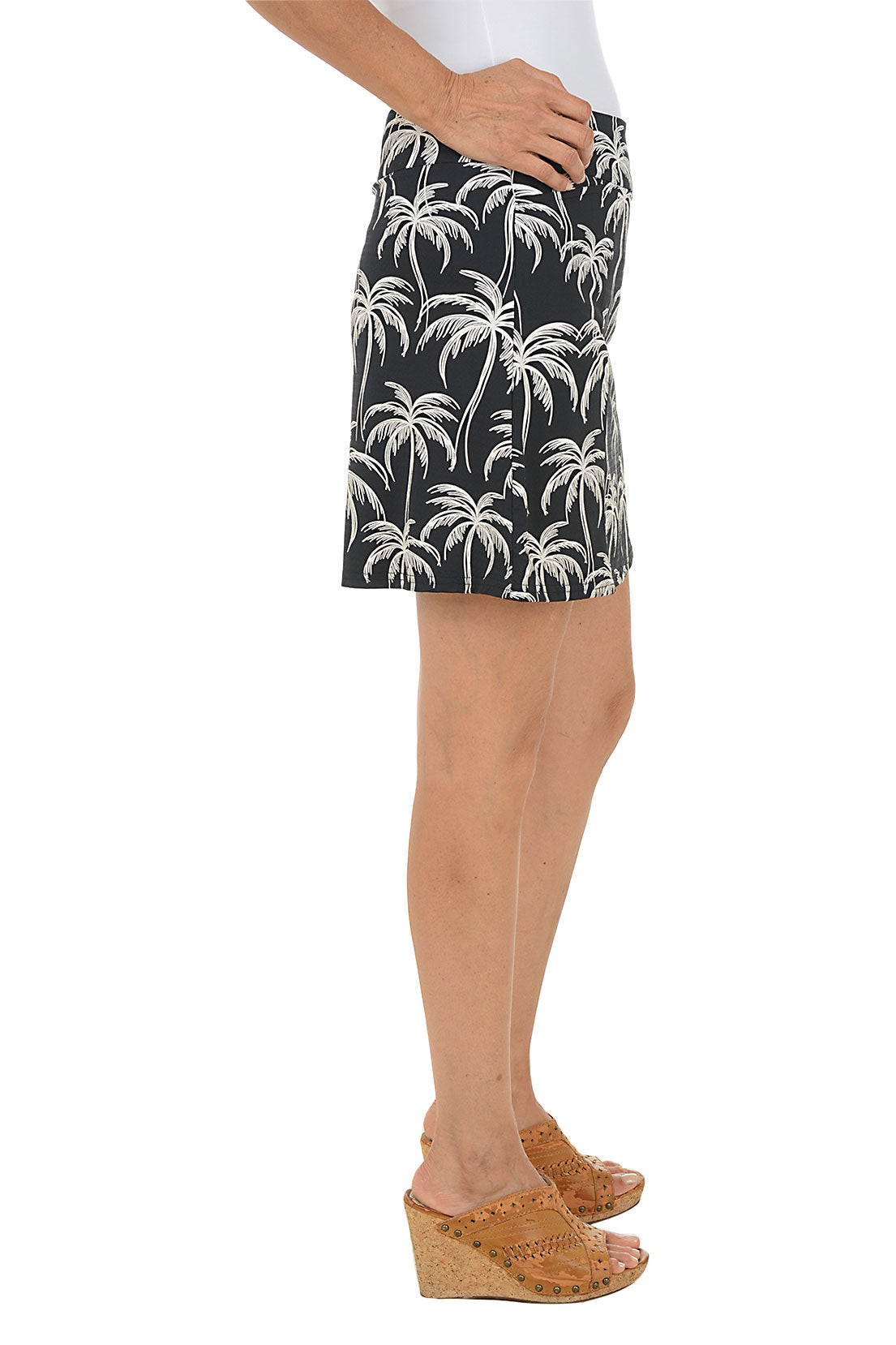 Person wearing a black skirt with palm tree pattern on a white background. Side shot.