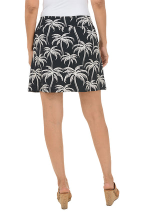 Person wearing a black skirt with white palm tree pattern on a plain background. Back shot.
