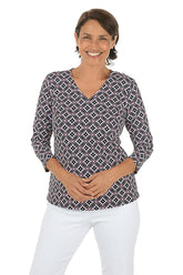 Woman wearing a black and white patterned top and white pants on a white background.