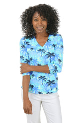 Woman wearing a blue palm tree patterned blouse on a white background.