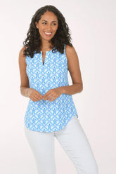 Woman wearing a blue patterned sleeveless top and white pants on a white background