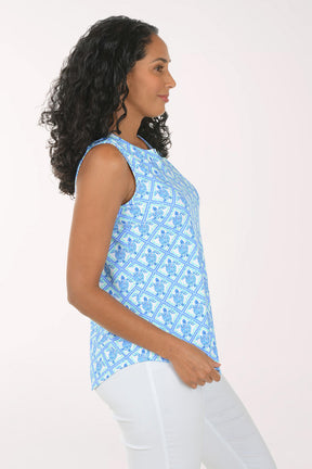 Woman wearing a blue patterned sleeveless top and white pants on a white background