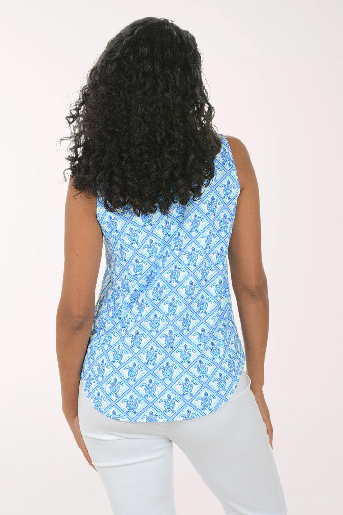 Woman wearing a blue patterned sleeveless top and white pants on a white background