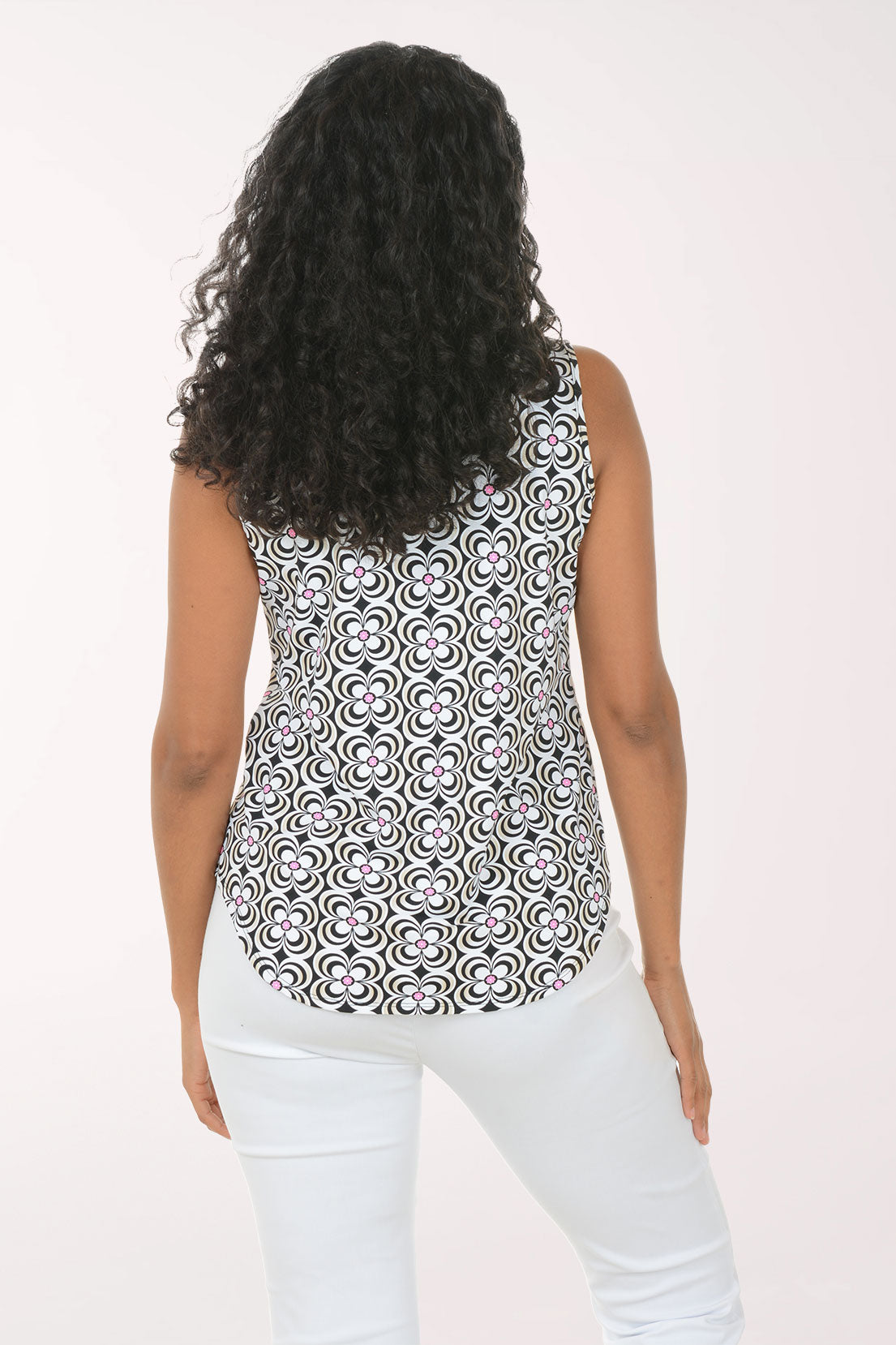 Woman wearing a sleeveless patterned top and light blue jeans on a white background