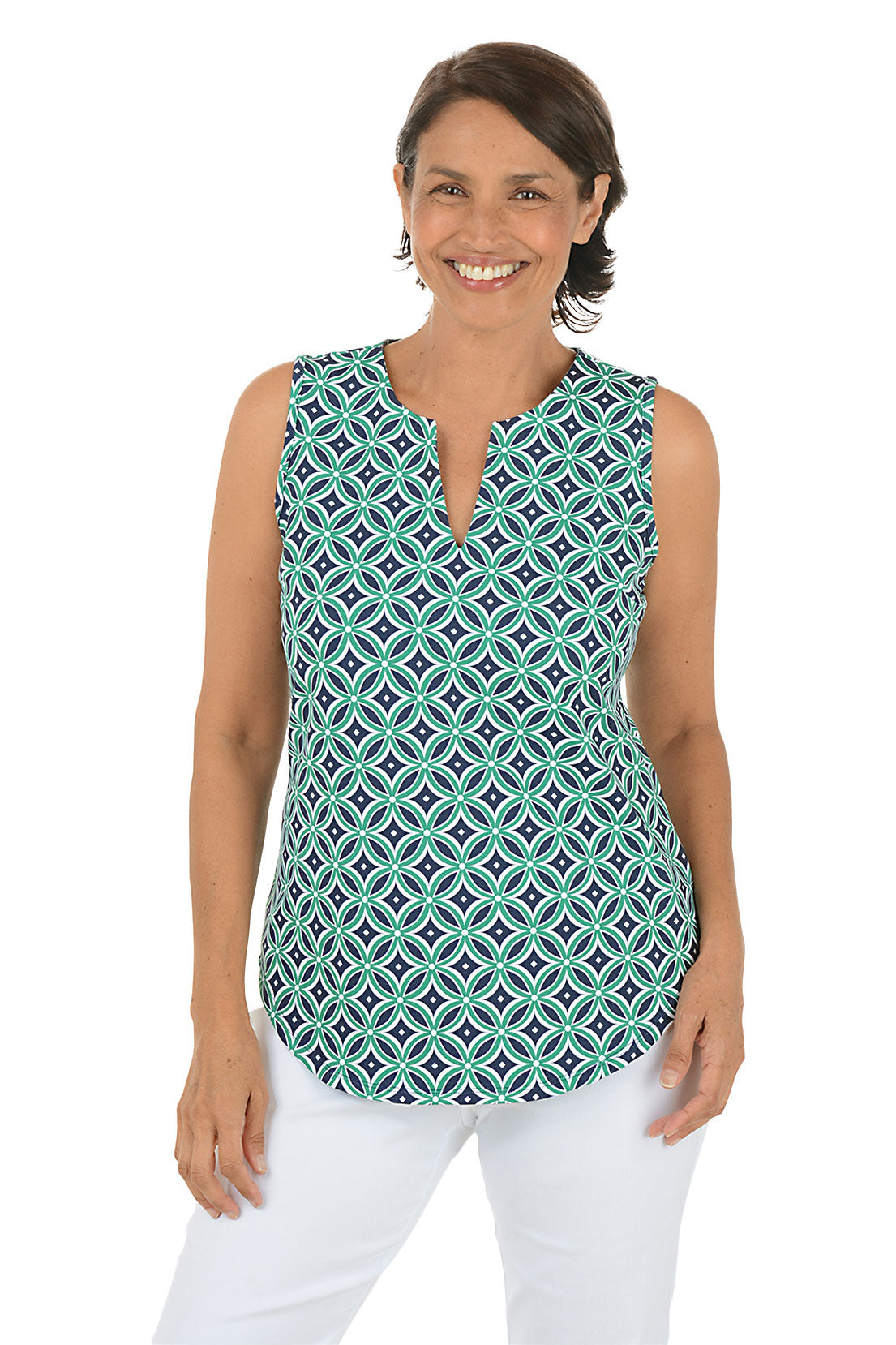 Woman wearing a navy and green sleeveless patterned top with white pants on a white background.