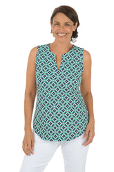 Woman wearing a navy and green sleeveless patterned top with white pants on a white background.
