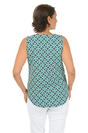 Woman wearing a navy and green sleeveless patterned top and white pants on a white background. Back shot.