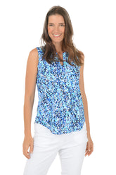 Woman wearing a blue floral sleeveless top and white pants on a white background.