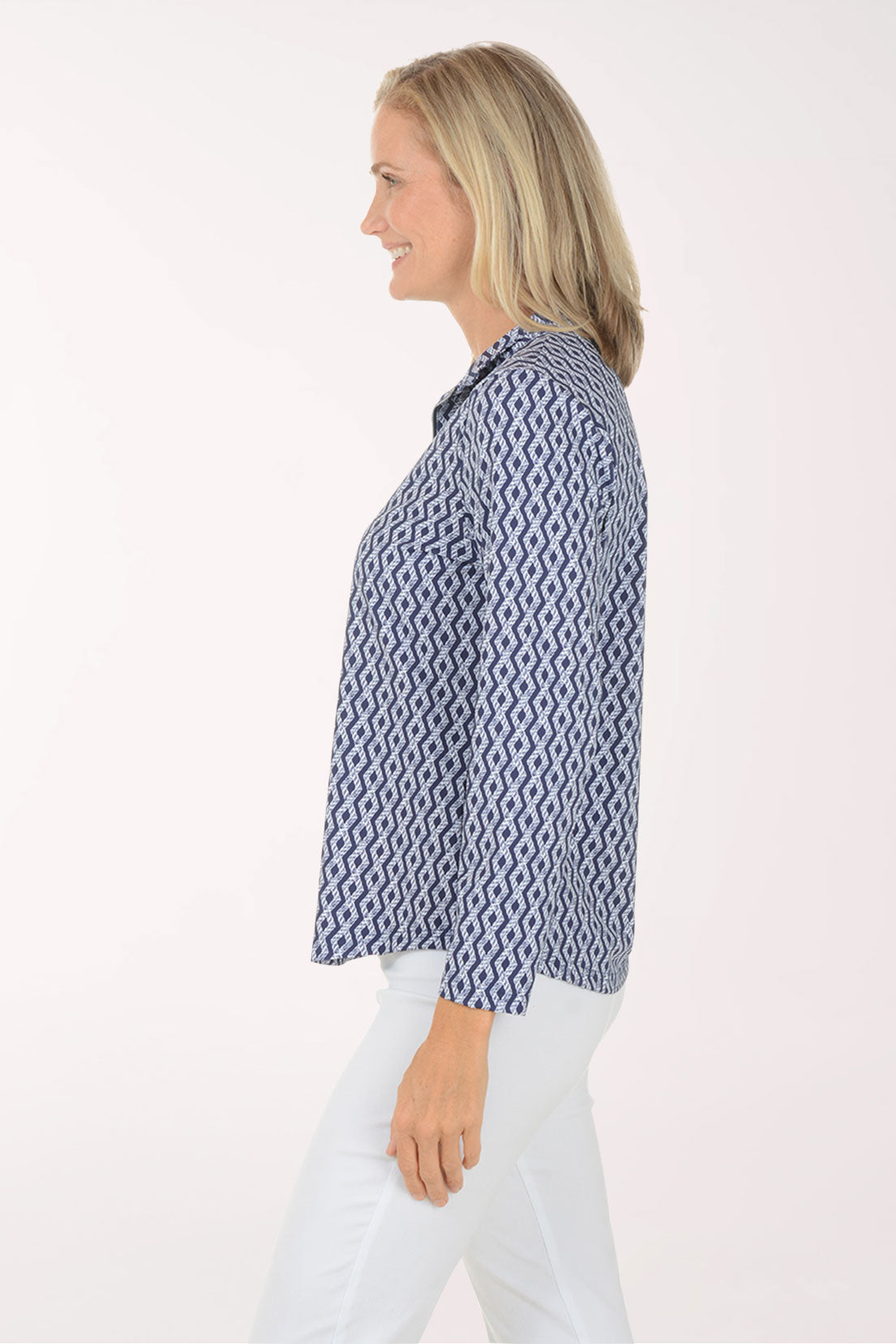 Woman wearing a blue patterned long-sleeve shirt and white pants on a white background