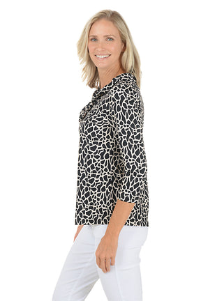 A woman wearing a 3/4 sleeve black and white giraffe pattern top with a v-neck ruffle neckline. Side shot.