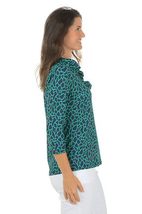 Woman wearing a teal leopard print shirt and white pants on a white background. Side shot.