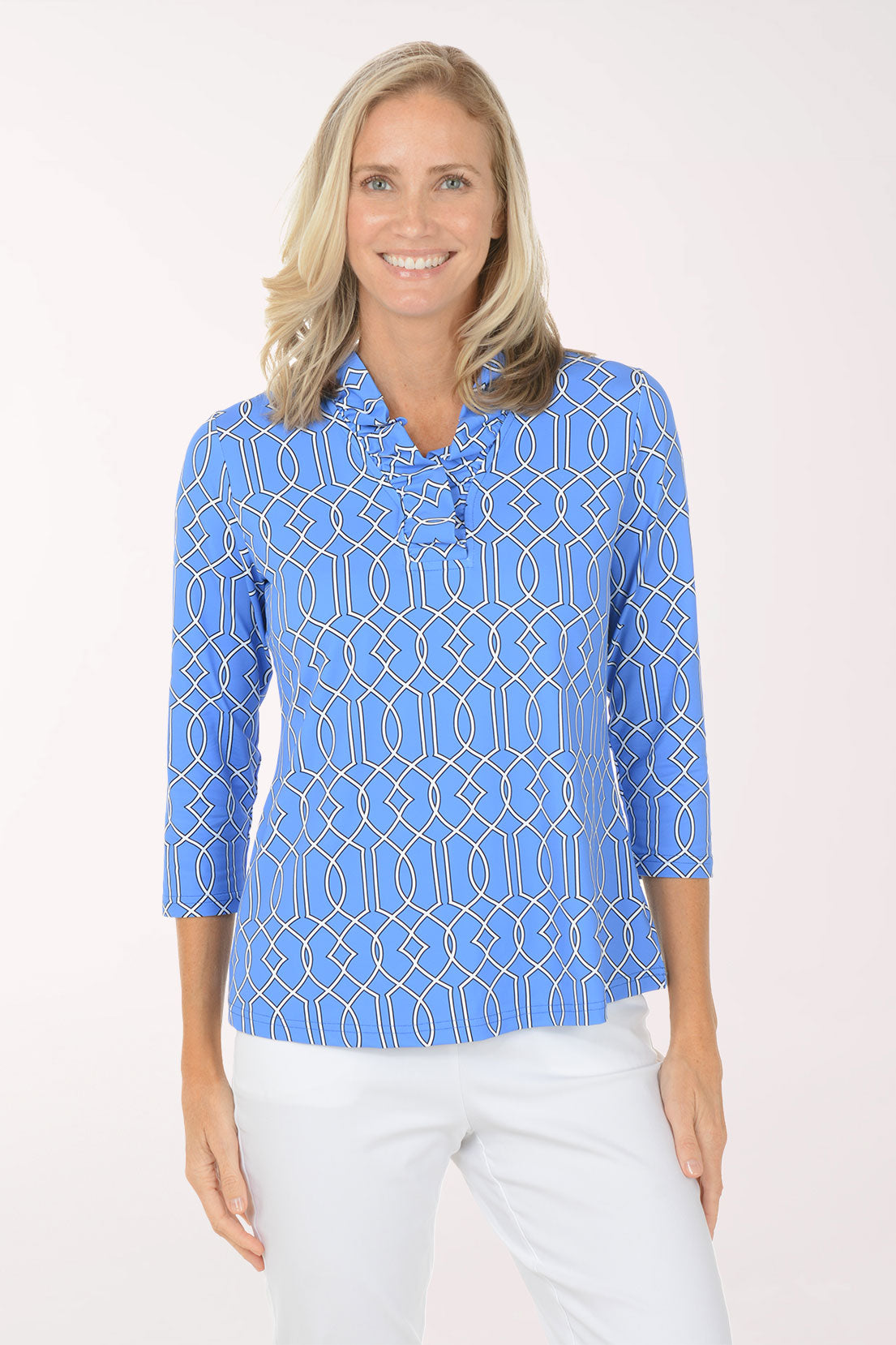 Woman wearing a blue patterned shirt with white pants on a light pink background