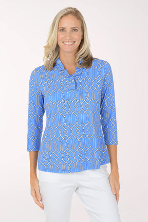 Woman wearing a blue patterned shirt with white pants on a light pink background