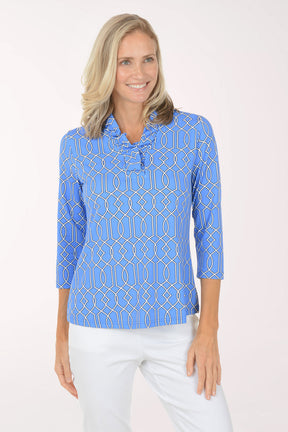 Woman wearing a blue patterned shirt with white pants on a light pink background