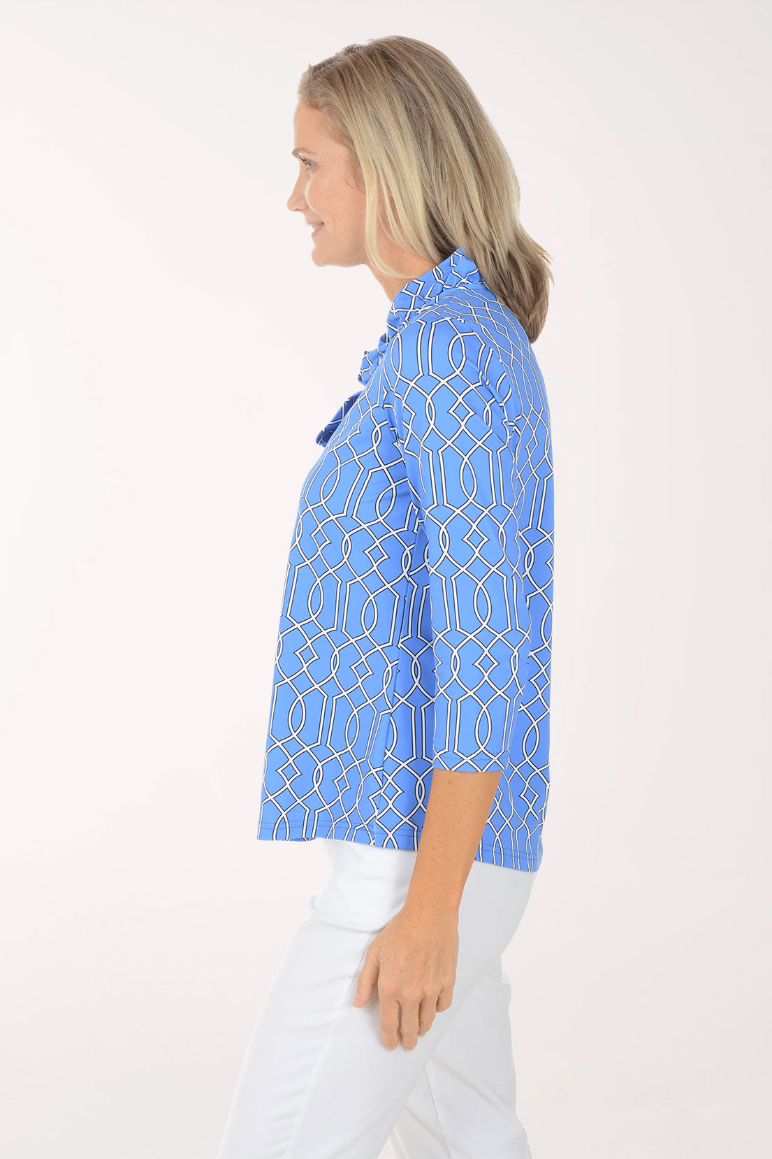 Woman wearing a blue patterned shirt with white pants on a light pink background