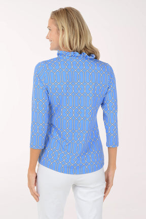 Woman wearing a blue patterned shirt with white pants on a light pink background