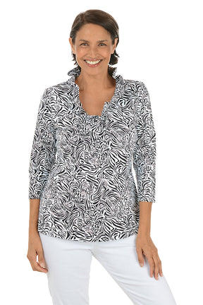 Woman wearing a black and white patterned blouse with white pants on a white background.