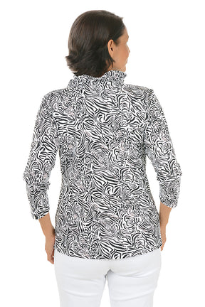 Woman wearing a black and white patterned blouse with white pants on a white background. Back shot.