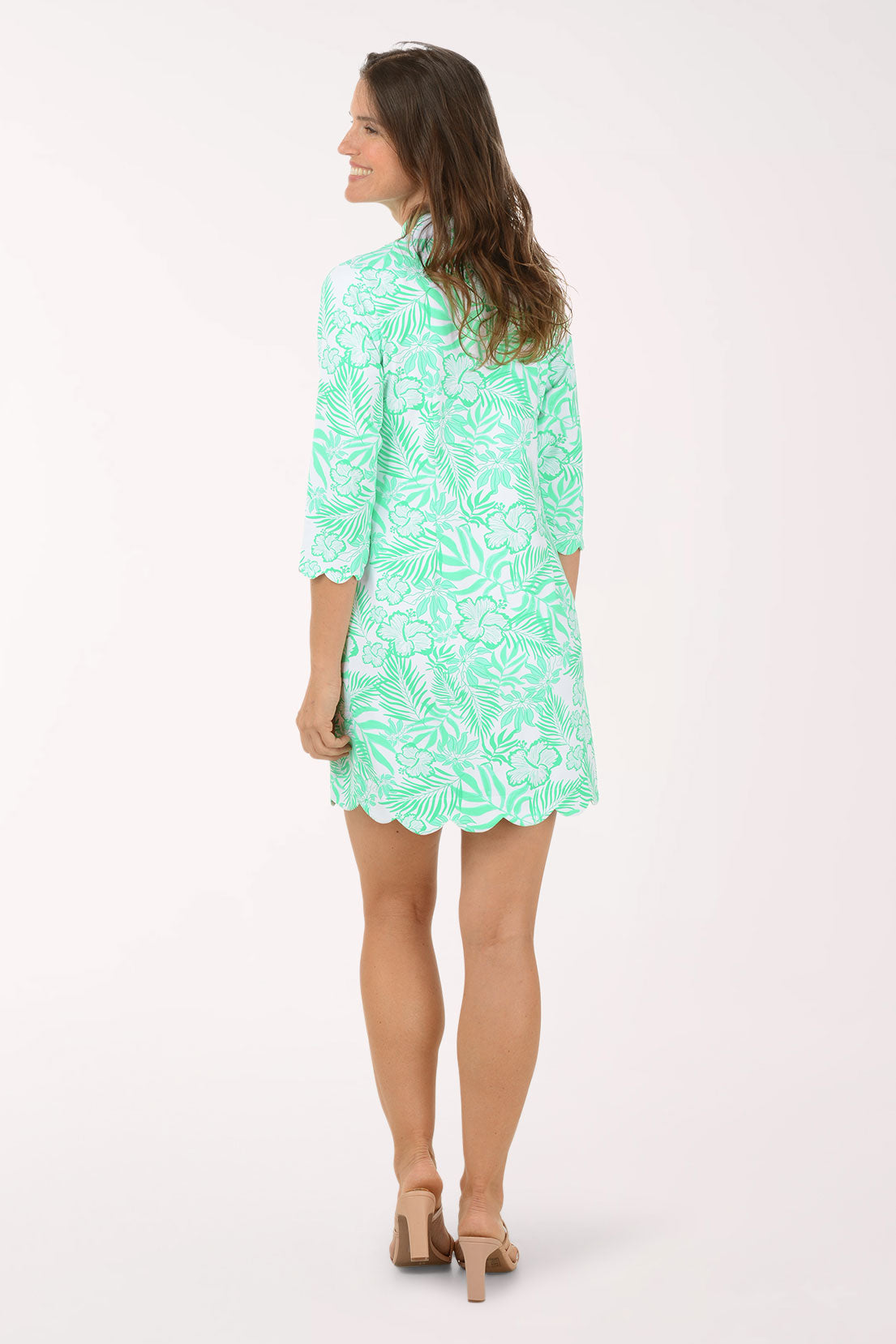 Woman wearing a green patterned dress on a white background. Back shot.