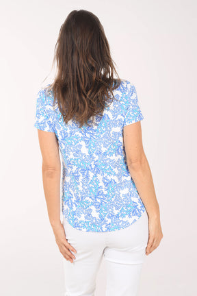 Woman wearing a blue floral blouse and white pants on a white background