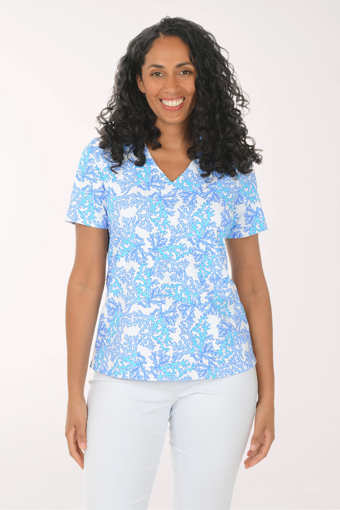 Woman wearing a blue patterned top and white pants on a white background